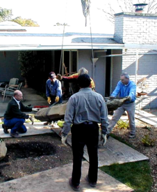 Large boulder placement brought over house by crane 